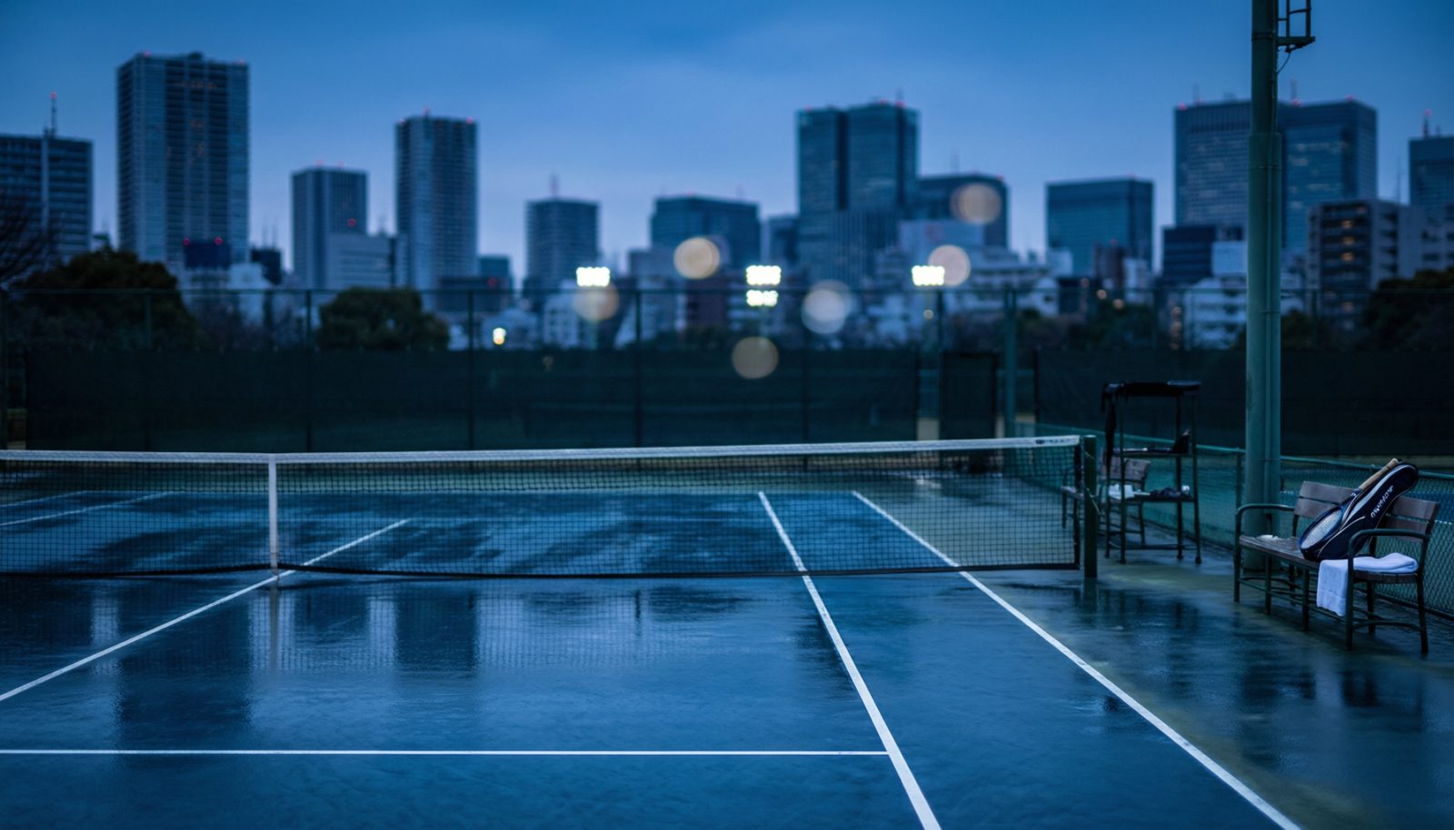 AI生成示意图:黄昏时分的室外硬地球场与场边空椅,远处是城市灯光
